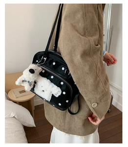 Detailed side view of black polka dot shoulder bag with a cute white puppy plush charm