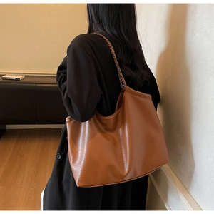 Model wearing a caramel brown PU leather tote bag with a stylish metal chain strap