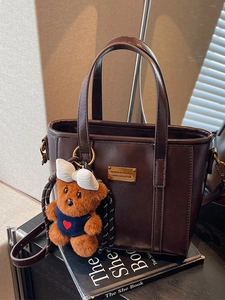 Deep brown faux leather tote bag with plush bear charm on black book base