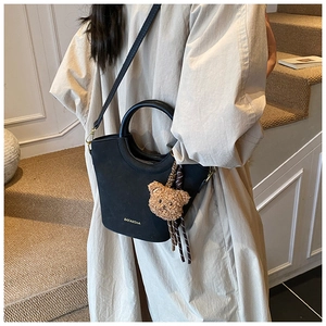 Détail du sac seau noir en PU mat avec poignée ronde, logo doré et breloque ours en peluche