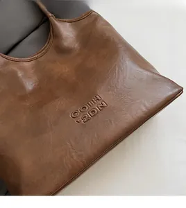 Gros plan d'un sac cabas marron en similicuir avec texture souple et logo embossé