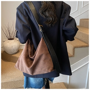 Detail of dark brown suede crossbody bag with black leather strap and gold buckle