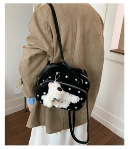 Polka dot shoulder bag with plush puppy pendant shown from a side-view on a model