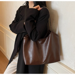 Detail of a large brown hobo tote bag with a chain strap on a model shoulder