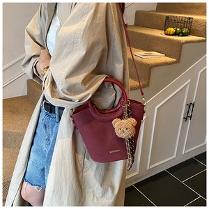 Détail d'un sac seau bordeaux vintage avec un ours en peluche et un foulard à carreaux
