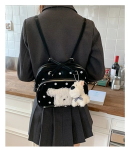 Detail of black polka dot backpack featuring a plush white puppy charm and leather texture