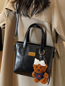 Stylish black leather tote bag for women with gold hardware and a cute plush bear charm