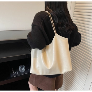 Minimalist cream tote bag with metal chain strap and pebble leather texture shown on model