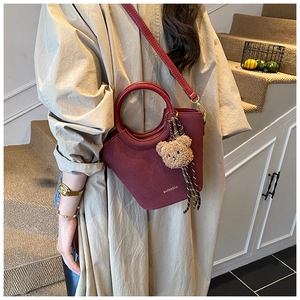 Détail du sac seau en cuir rouge avec breloque ours en peluche et bandoulière longue