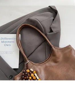 Gros plan d'un sac cabas en cuir marron avec pompon en perles de bois sur blazer gris