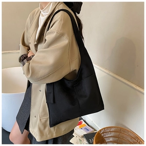 Close-up of minimalist black canvas tote bag with front pocket worn with a beige coat