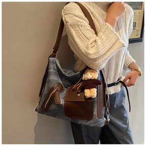 Detail view of large blue canvas tote bag with brown leather pockets and a cute bear charm