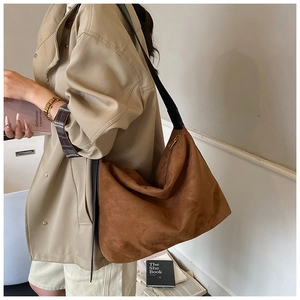 Detailed side view of a brown suede hobo bag with wide black shoulder strap and top zipper