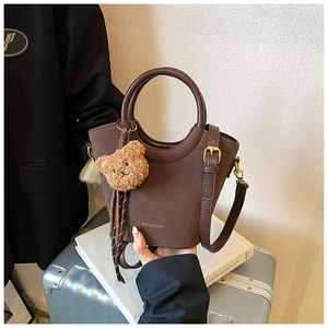 Détail d'un sac seau en daim marron foncé avec quincaillerie dorée et ours en peluche