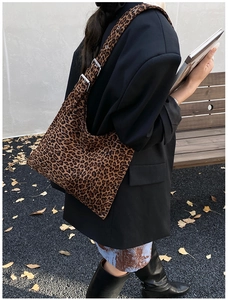 Detail of leopard print shoulder bag featuring metallic eyelets and wide strap on autumn park bench