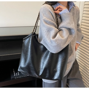Detail of black wax texture tote bag with metal chain strap and minimalist logo