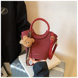 Détail du sac seau en daim rouge avec logo BAFANSHA et accessoire ours en peluche