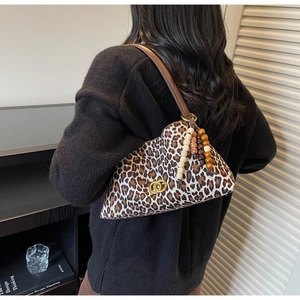 Detail of leopard print underarm bag with beaded charm and golden buckle on brown strap