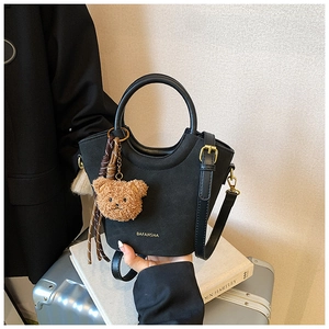 Détail du sac seau noir mat avec bandoulière réglable et accessoire d'ours en peluche