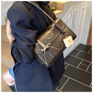 Détail d'un sac à bandoulière en cuir marron vintage avec un charm biscuit et un ruban