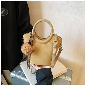 Détail du sac seau en daim camel avec poignée ronde et breloque ours en peluche