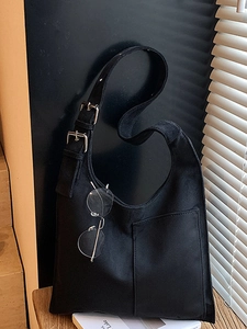 Minimalist black canvas hobo bag with adjustable silver buckles on a wooden stool