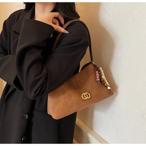 Detail of suede shoulder bag with golden logo and bohemian beaded tassel fringe