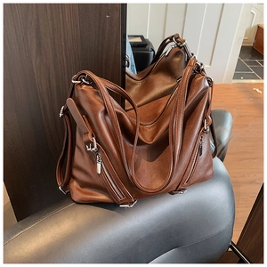 Close-up of brown textured leather tote bag with metal zipper and adjustable strap details