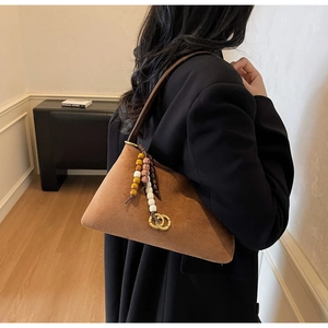 Detail view of brown suede underarm bag with ethnic beads and gold rings on black coat