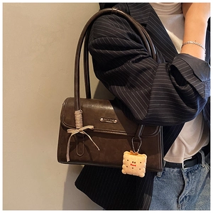 Détail d'un sac à bandoulière marron vintage avec nœud décoratif et pendentif biscuit