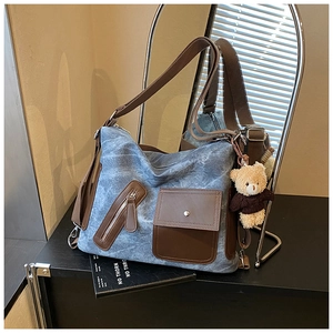 Close-up of vintage denim tote bag with leather trim and a cute plush bear charm