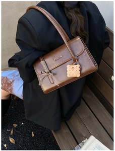 Détail d'un sac baguette marron avec nœud à carreaux et breloque en peluche biscuit