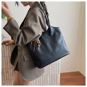 Détail du sac cabas en cuir noir avec lettres embossées et breloque en perles de bois