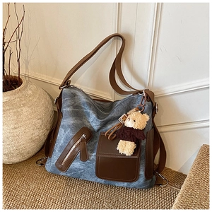 Blue denim tote bag with brown leather straps and a small bear charm on a woven rug