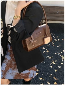 Sac sous le bras vintage marron avec nœud rayé et breloque biscuit sur un chemin