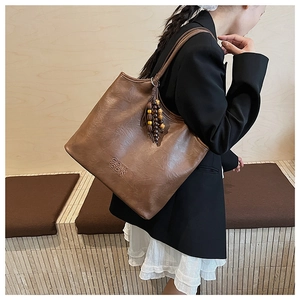Détail d'un sac cabas marron montrant le grain du cuir, perles en bois et logo gravé