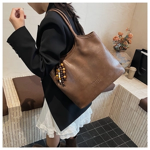 Détail du grand sac cabas en cuir marron foncé avec perles en bois et logo embossé