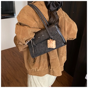 Détail d'un sac sous le bras en cuir noir rétro avec logo en métal et breloque peluche