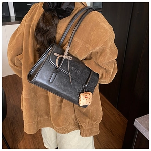 Détail d'un sac porté épaule vintage en cuir noir mat avec charm en peluche et un noeud