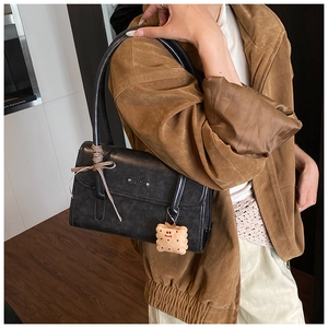 Détail d'un sac porté épaule en cuir noir avec ruban et pendentif biscuit en peluche