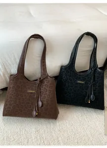 Détail de sacs cabas léopard avec texture en daim, logo en métal et breloque à pampilles