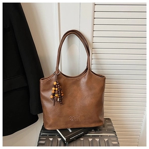 Détail d'un sac cabas en cuir marron avec franges perlées et logo sur une valise