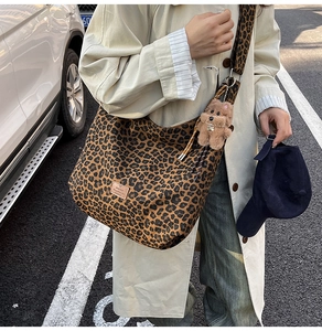 Close-up of leopard print canvas hobo bag with wide strap and plush dog pendant