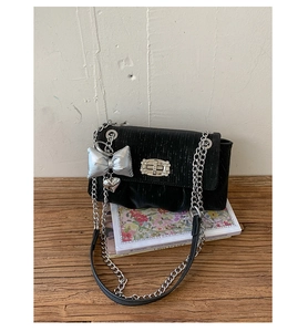 Detail of black textured square bag with silver chain, bow charm and heart pendant