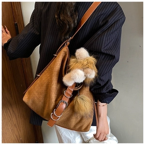 Detail of caramel brown woven tote bag with decorative buckle and plush pom-pom charm