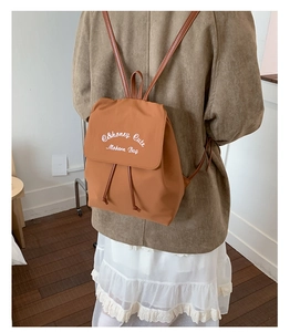 Sac à dos en nylon caramel avec cordon de serrage et broderie blanche porté par un mannequin