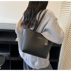 Close-up of black lychee grain leather tote bag with gold embossed logo and side tag