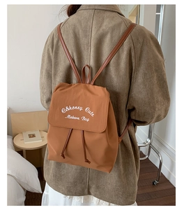 Détail des lettres brodées sur un sac à dos en tissu caramel avec fermeture à cordon