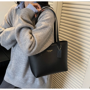 Detail of black lychee grain leather tote bag showing gold logo and decorative tag