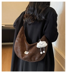 Detail of a brown suede crescent bag with a white brand label and plush cloud charm decor